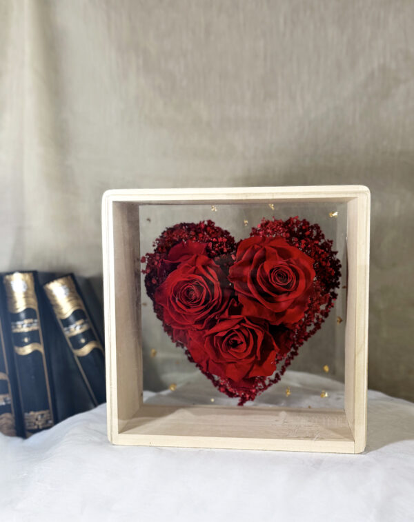 Composition de roses éternelles en cœur avec amarante rouge dans un cadre bois et plexiglas.